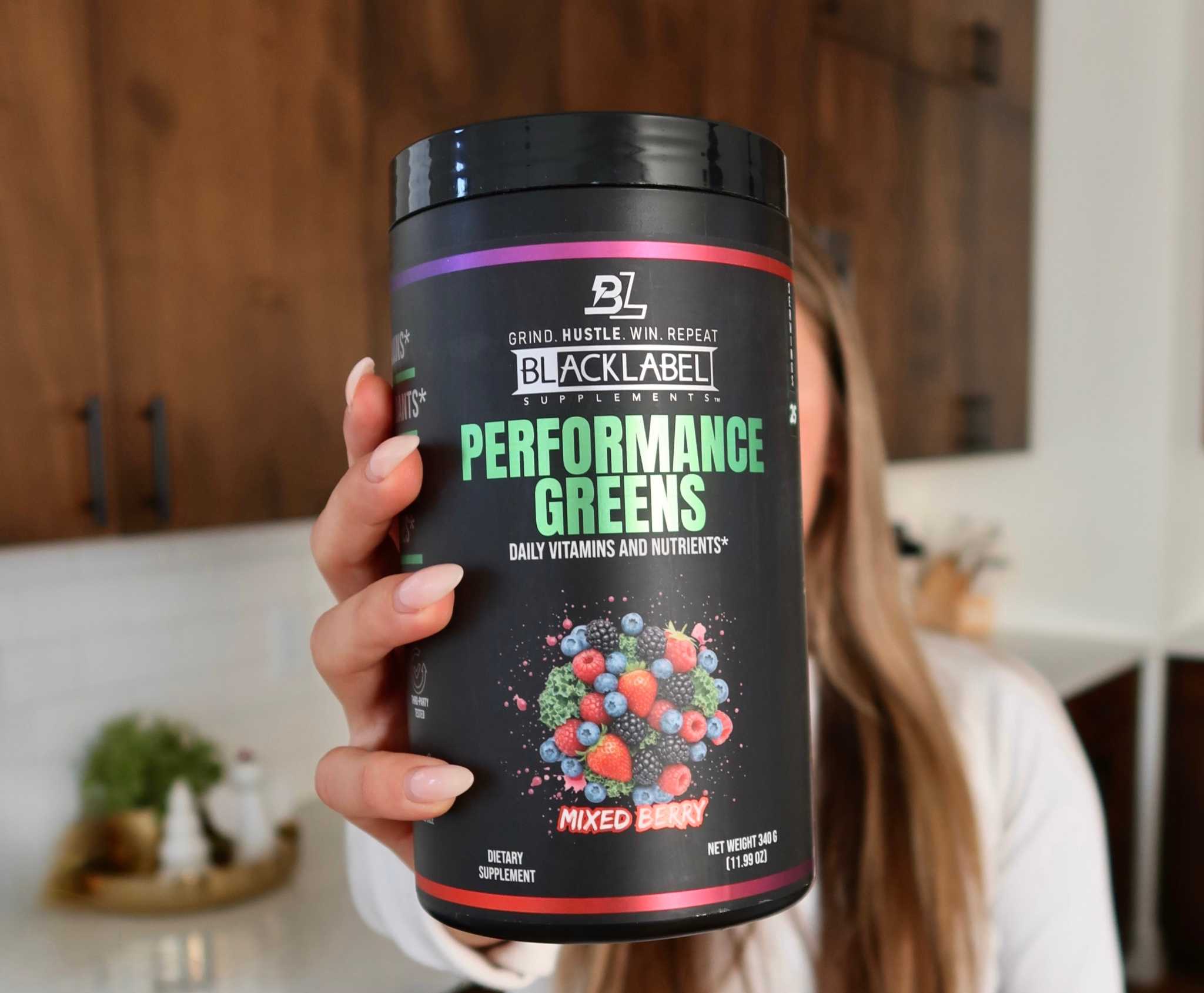 PERFORMANCE GREENS powder in a black tub with berry graphics, purple and red bands, and a black screw lid