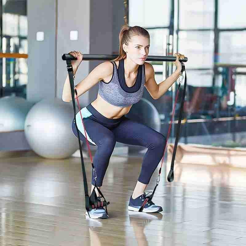 Pilates Bar Kit with black foam grip bar and red resistance bands used by woman in sportswear for home workout exercise.