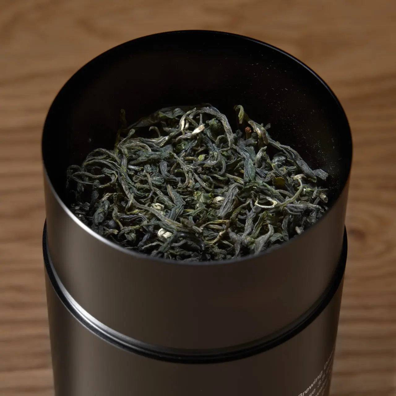 Premium Loose Leaf Tea in a brushed metal tin, featuring curled green tea leaves and an open-top design
