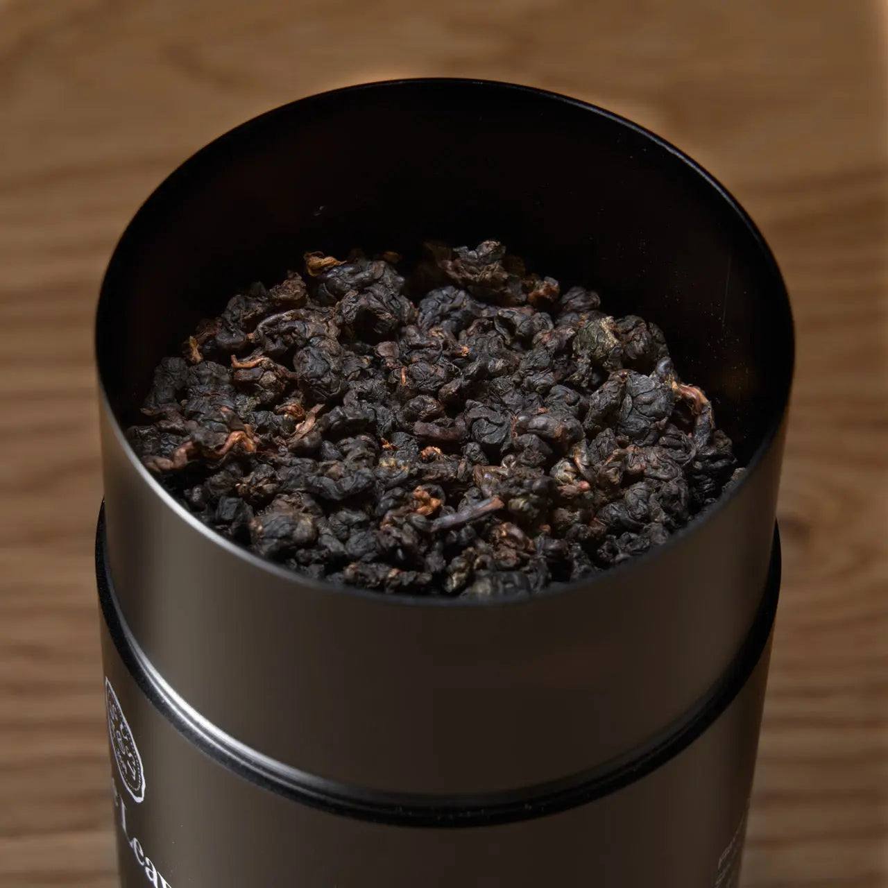Premium Loose Leaf Tea in a black metal tin, filled with dark, tightly rolled tea leaves