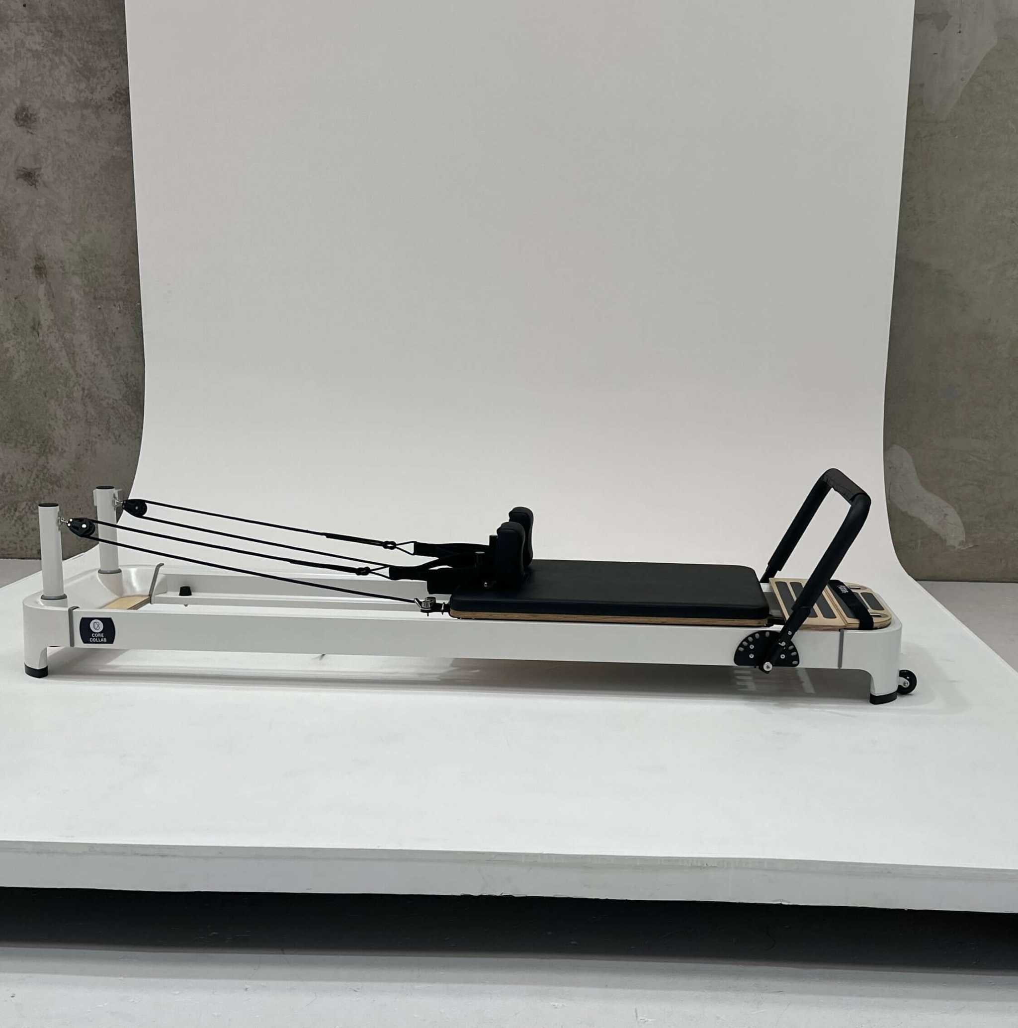 Queen 2.0 Studio Pilates Reformer in white with black padded carriage and adjustable footbar and ropes for resistance training