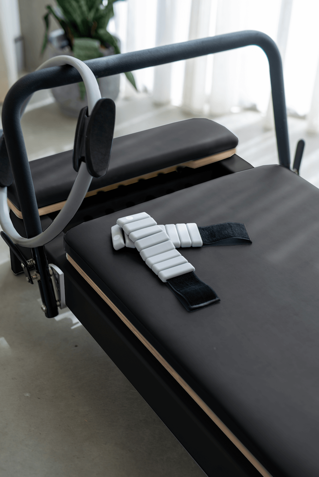 Queen Folding Reformer with black padded upholstery, grey frame, and attached white adjustable strap on carriage