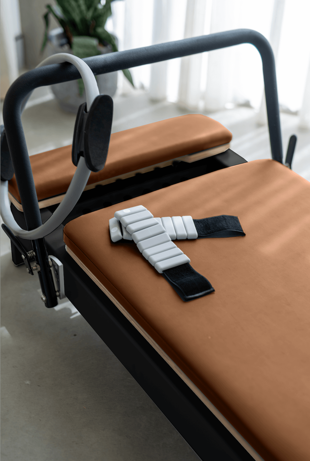 Queen Folding Reformer with brown padded upholstery, black metal frame, and attached gray resistance straps for Pilates workouts