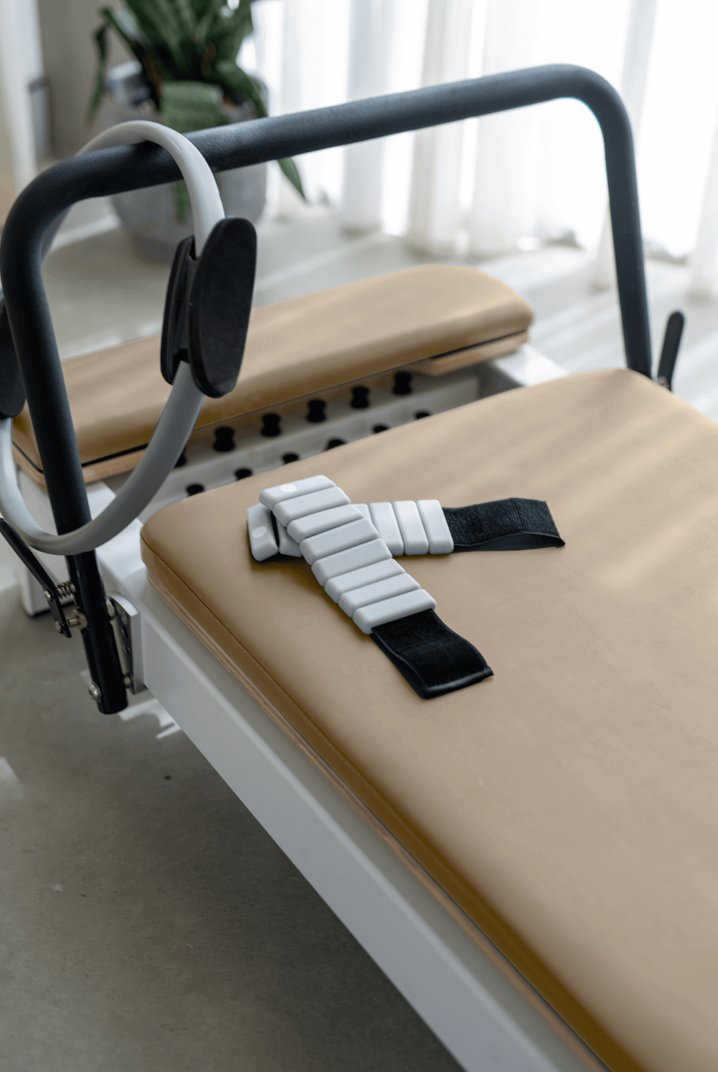 Queen Folding Reformer with beige upholstered padded platform, white metal frame, and attached gray Pilates ring accessory.