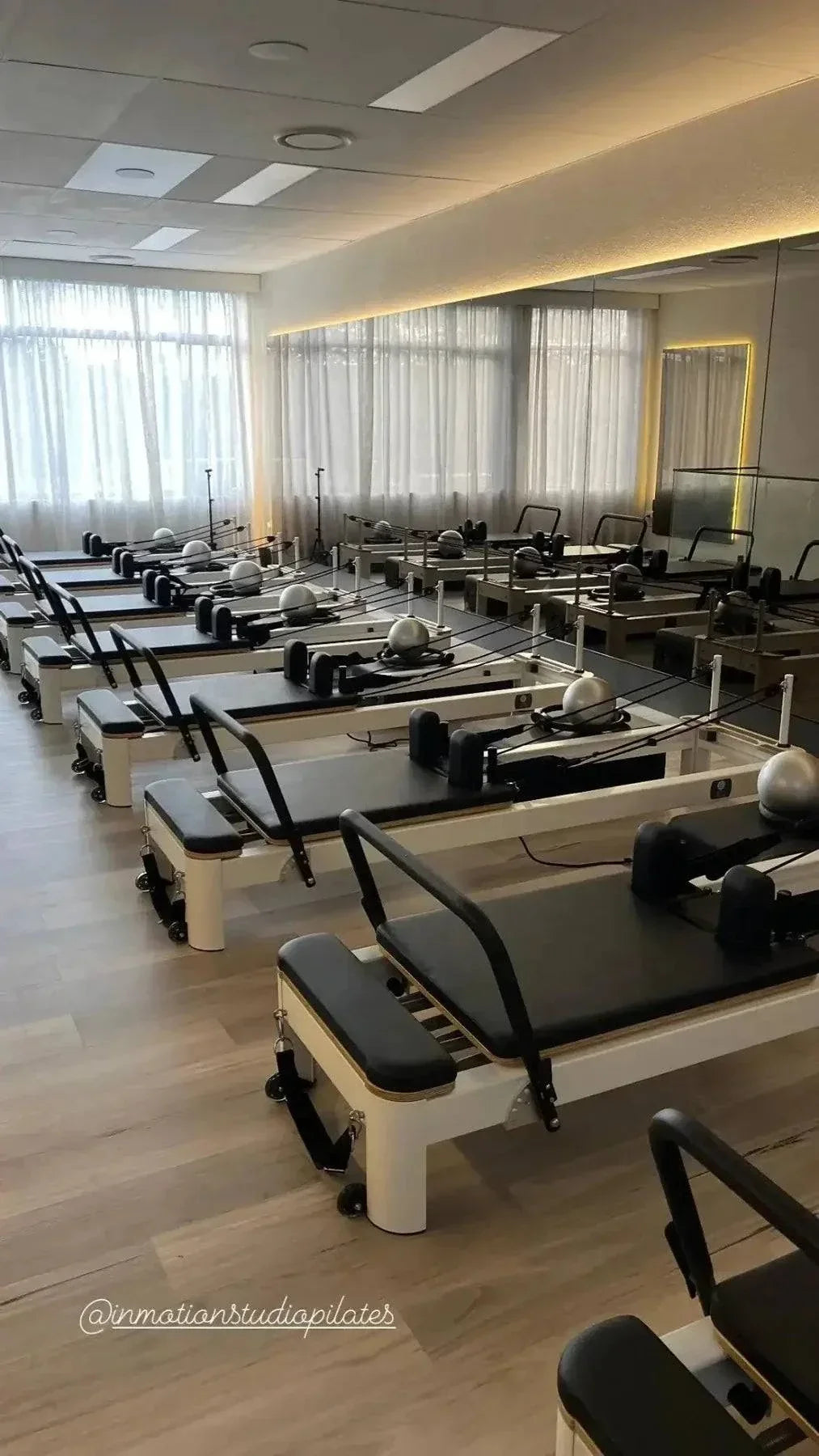Row of white-framed Queen Studio Pilates Reformer machines with black padded upholstery and adjustable ropes in a bright studio setting.