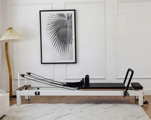 Queen Studio Pilates Reformer with white frame, black padded carriage, adjustable ropes, and sturdy footbar for professional exercise use.