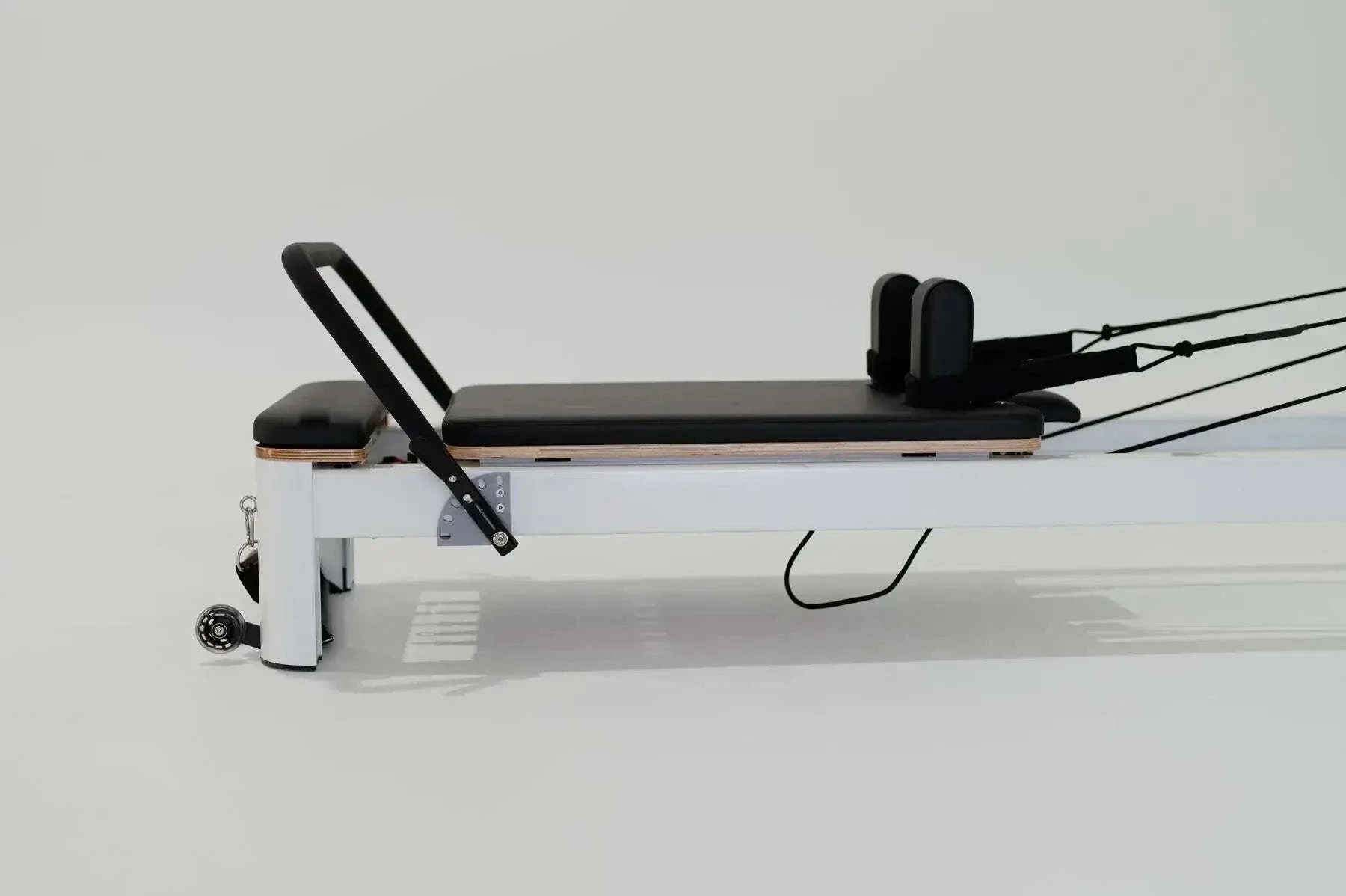 Queen Studio Pilates Reformer with white aluminum frame, black padded foam carriage, adjustable footbar, and resistance ropes for smooth glide.