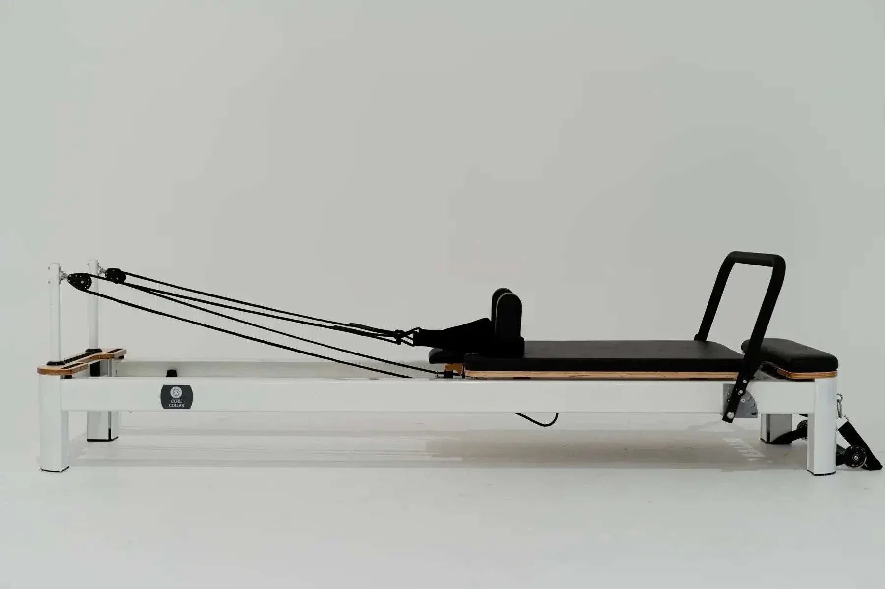 Queen Studio Pilates Reformer with white aluminum frame, black padded carriage, adjustable ropes, and footbar for professional use.