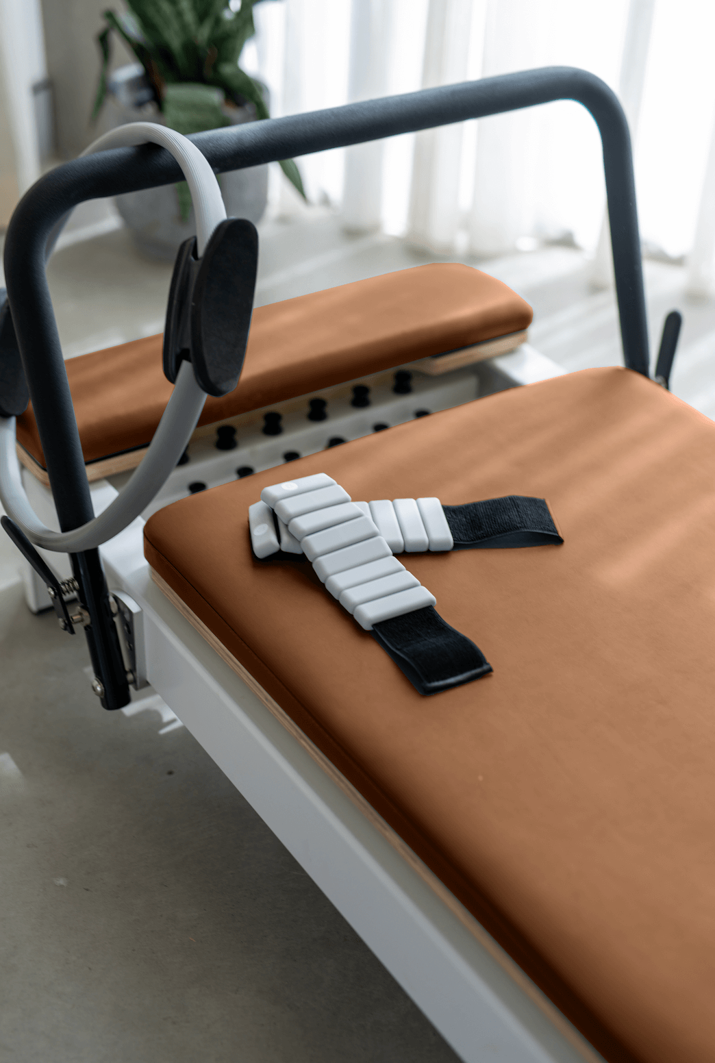 Queen Studio Reformer with brown padded leather surface, black strap, and metal frame in a minimalist design