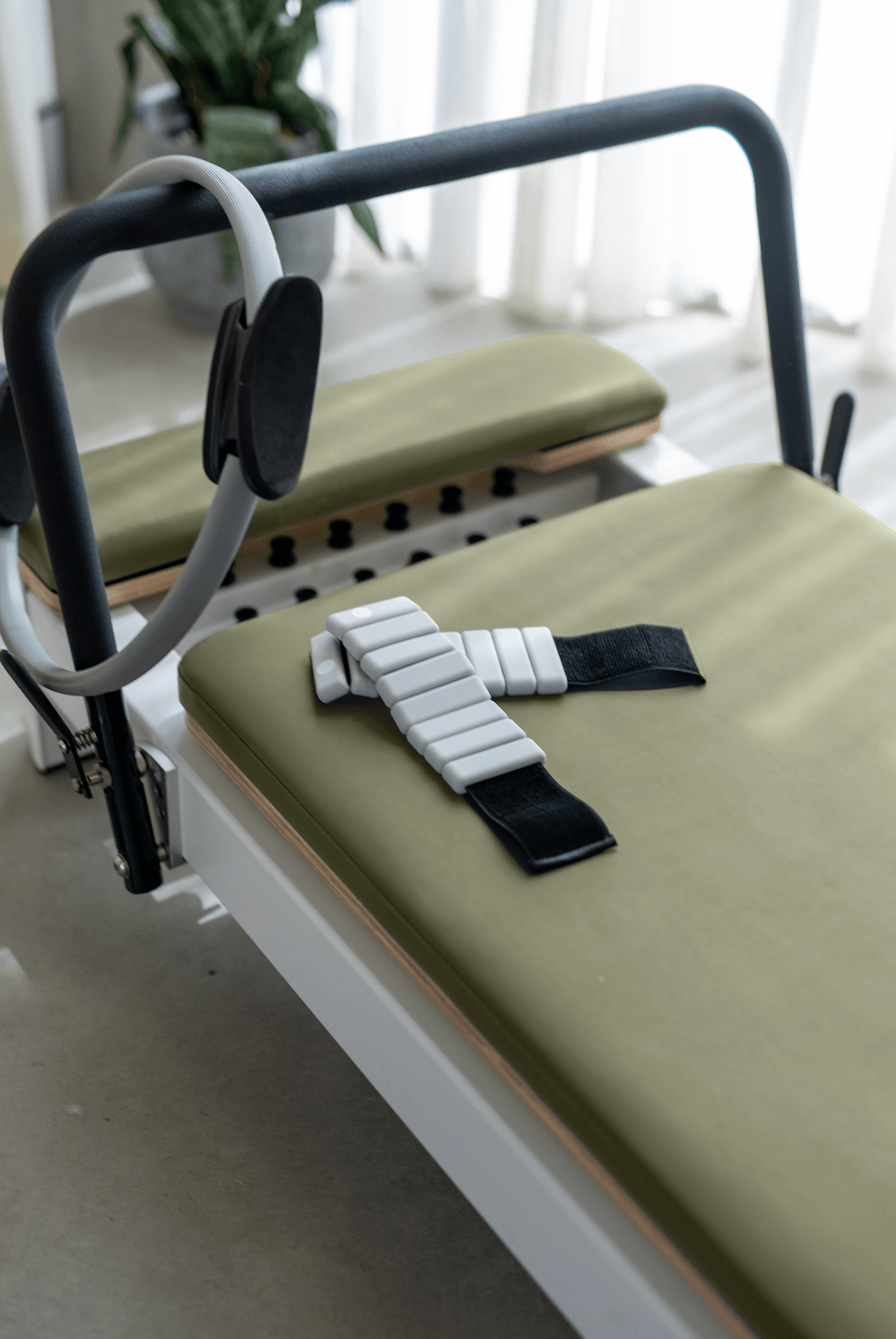Queen Studio Reformer Pilates machine with olive green cushions, black frame, white resistance straps, and smooth carriage