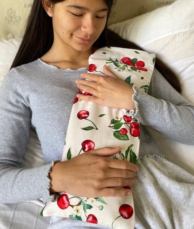 Rectangle/Cervical Pillow in cream fabric with a red cherry and green leaf print, held against the chest