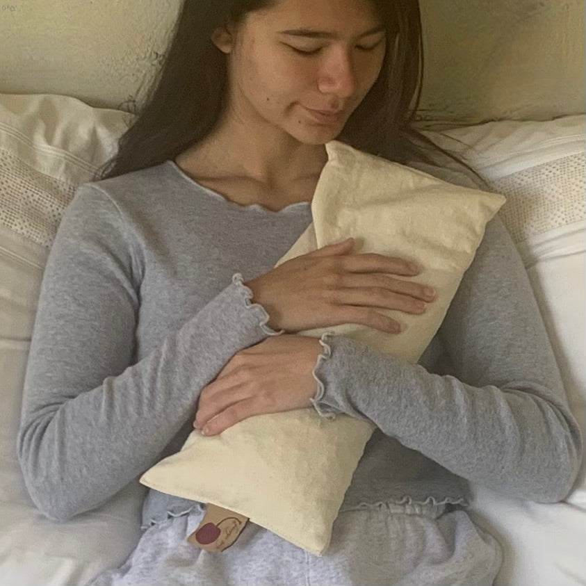 Rectangle/Cervical Pillow in natural unbleached denim, with a cream pillowcase, held against the chest