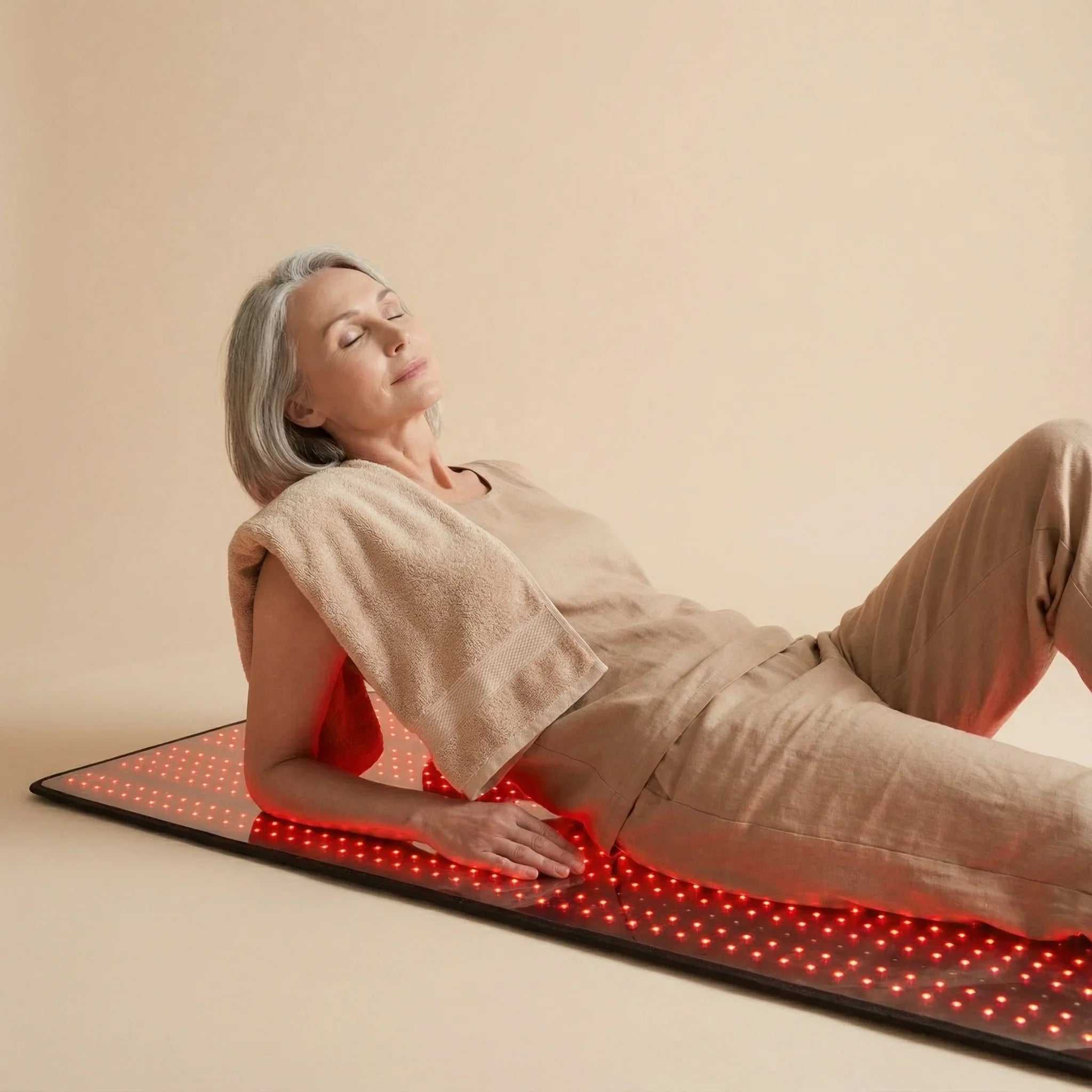 Red Light Therapy Mat with glowing red LEDs, black surface, and flexible full-body design shown beneath a reclining woman