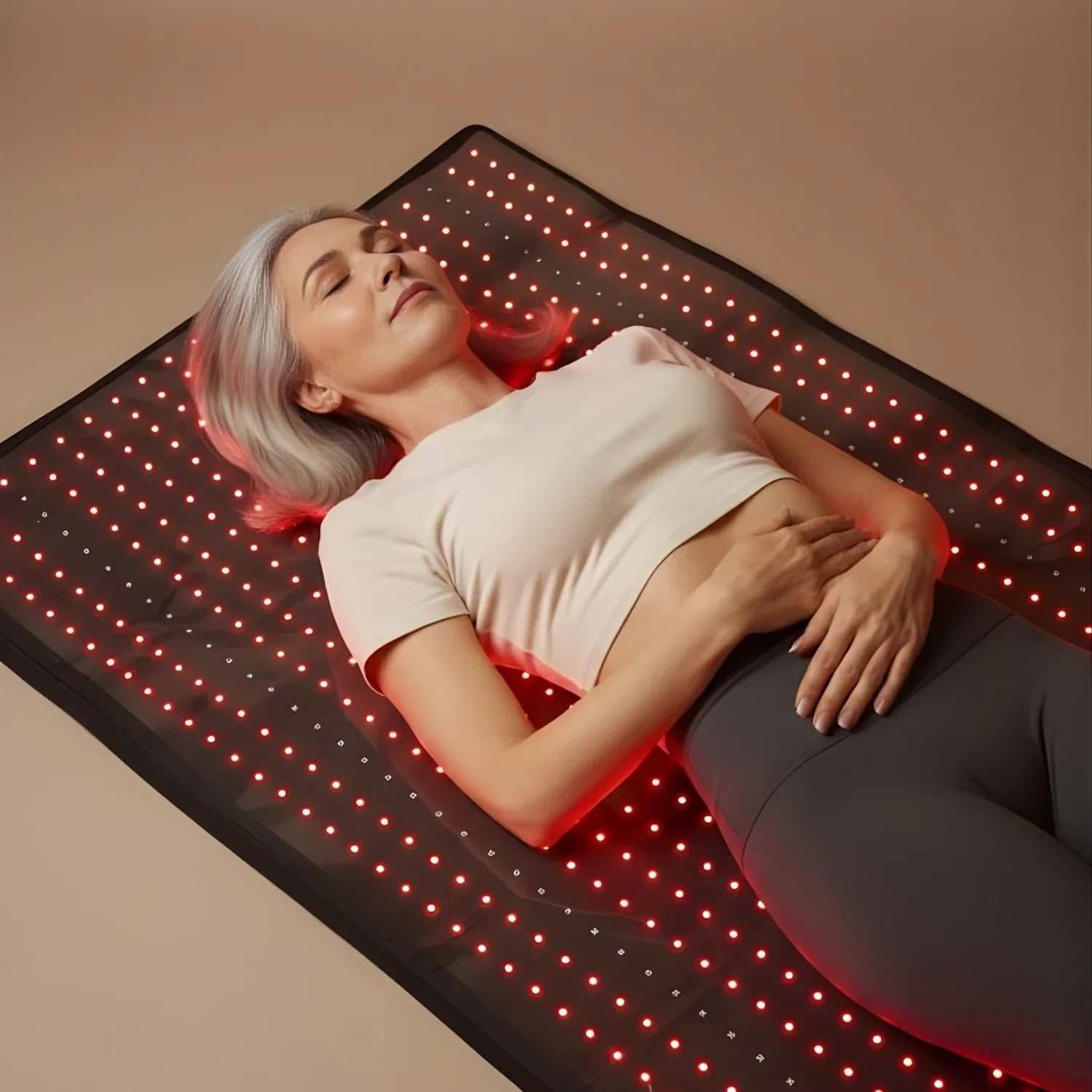 Red Light Therapy Mat with black flexible surface and glowing red LED lights used by a woman lying down