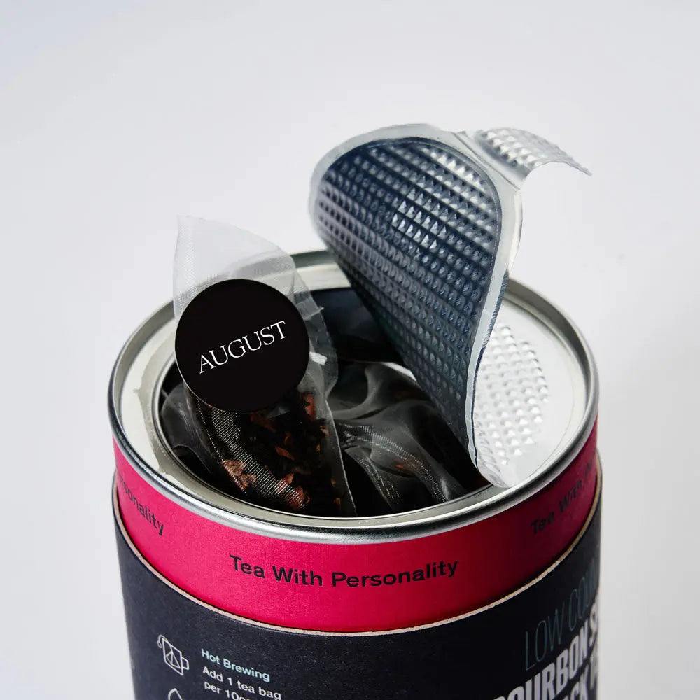 Roasted Pumpkin Caramel Rooibos Tea in a round black-and-pink tin, with a metal lid and individually wrapped tea bags
