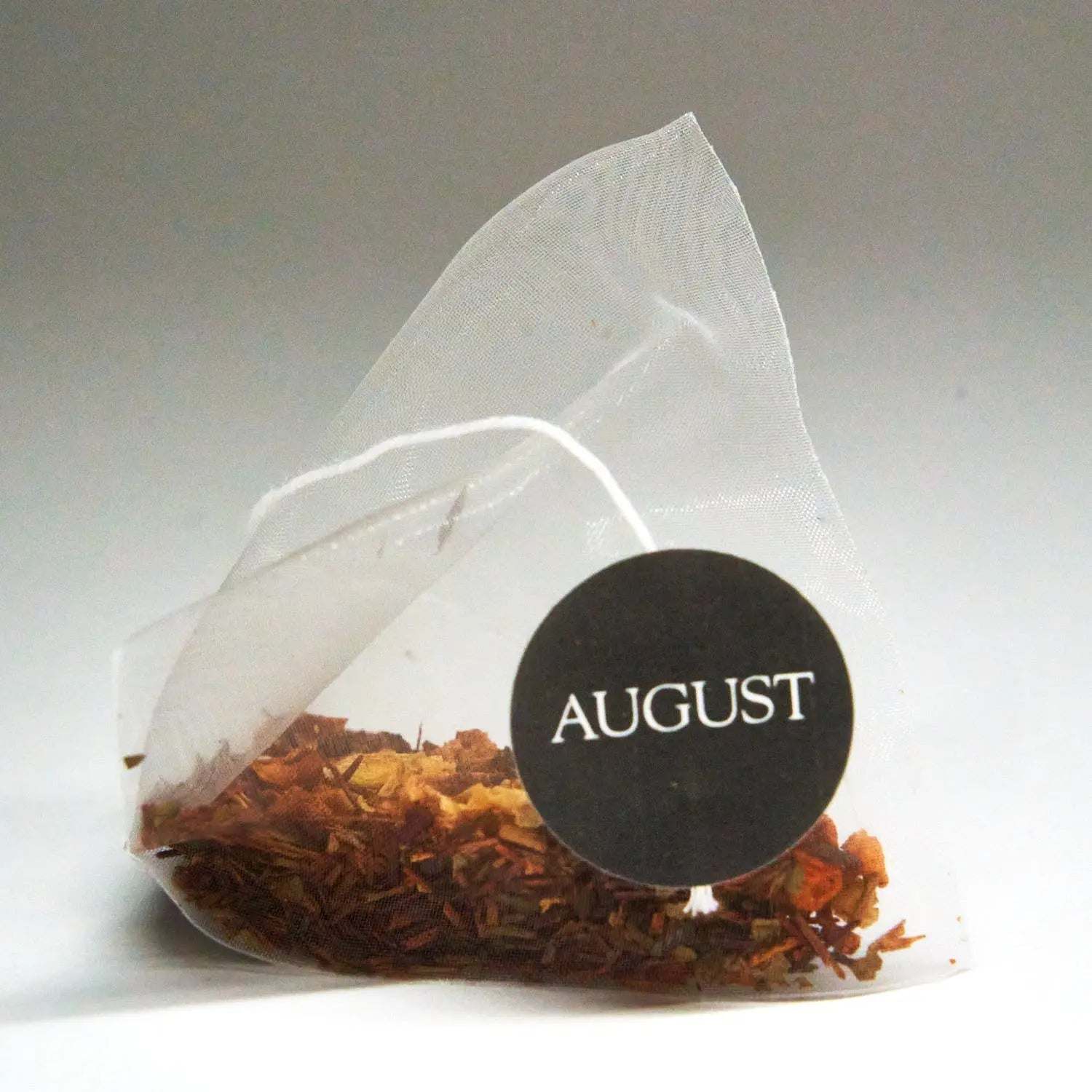 Roasted Pumpkin Caramel Rooibos Tea in a clear pyramid tea bag, showing loose reddish-brown tea and pumpkin pieces