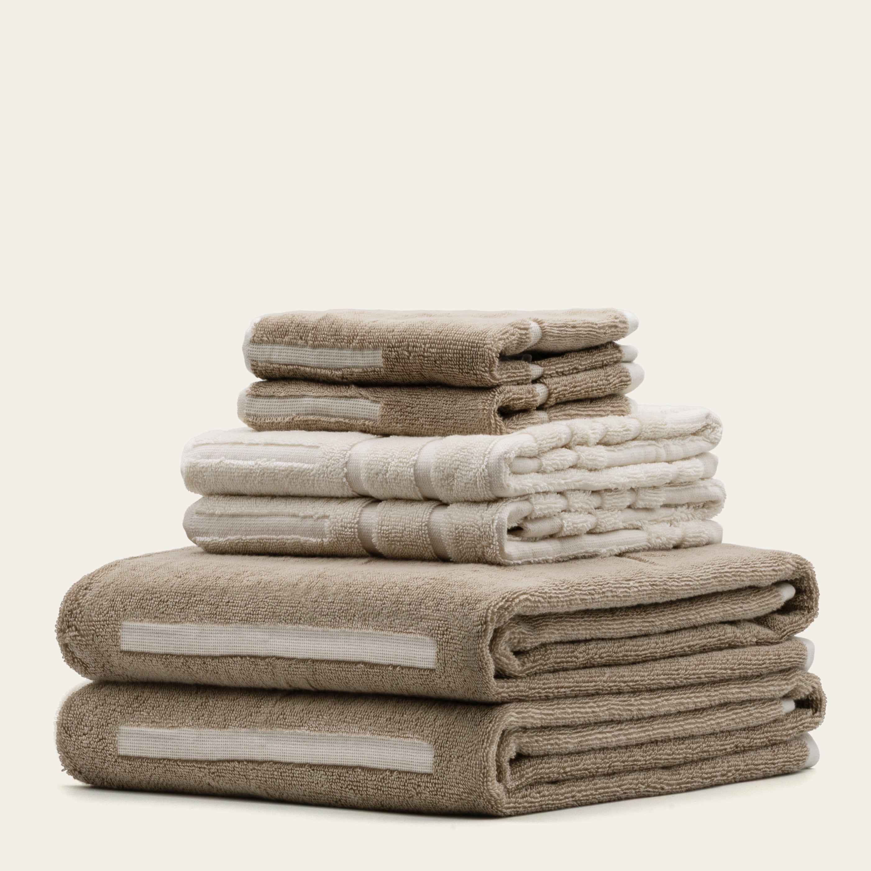 Sorrel Australian Cotton towels in sand and cream tones, stacked with plush texture and subtle woven border stripes