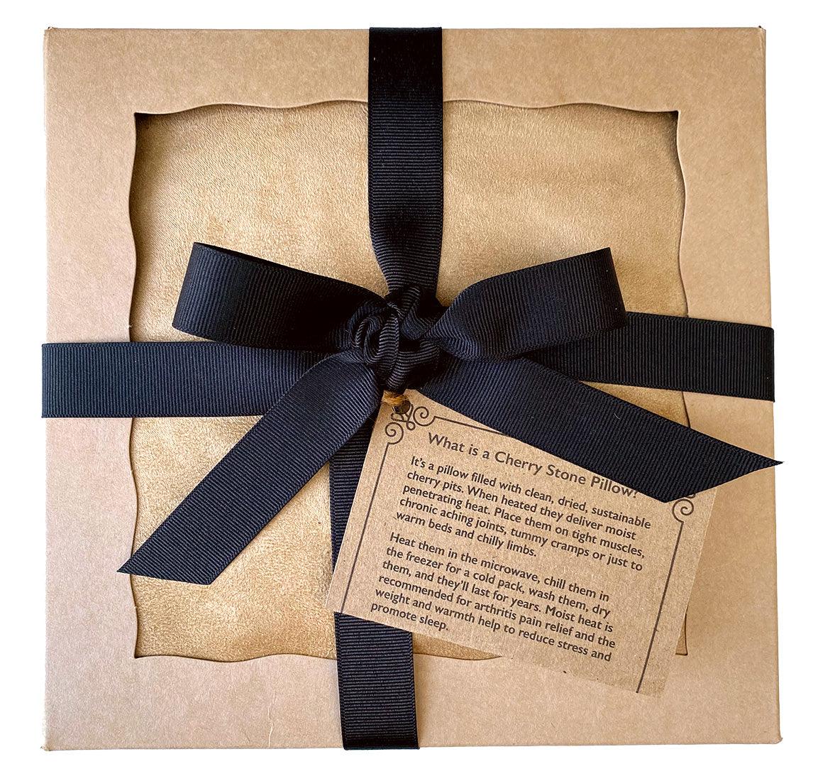Square Cherry Stone Pillow in tan suede fabric, packaged in a kraft box with a wide black ribbon and product card
