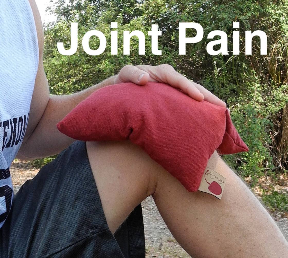 Summer Stack red square denim pain-relief pillow with a soft fabric cover, held against a bent knee for joint pain