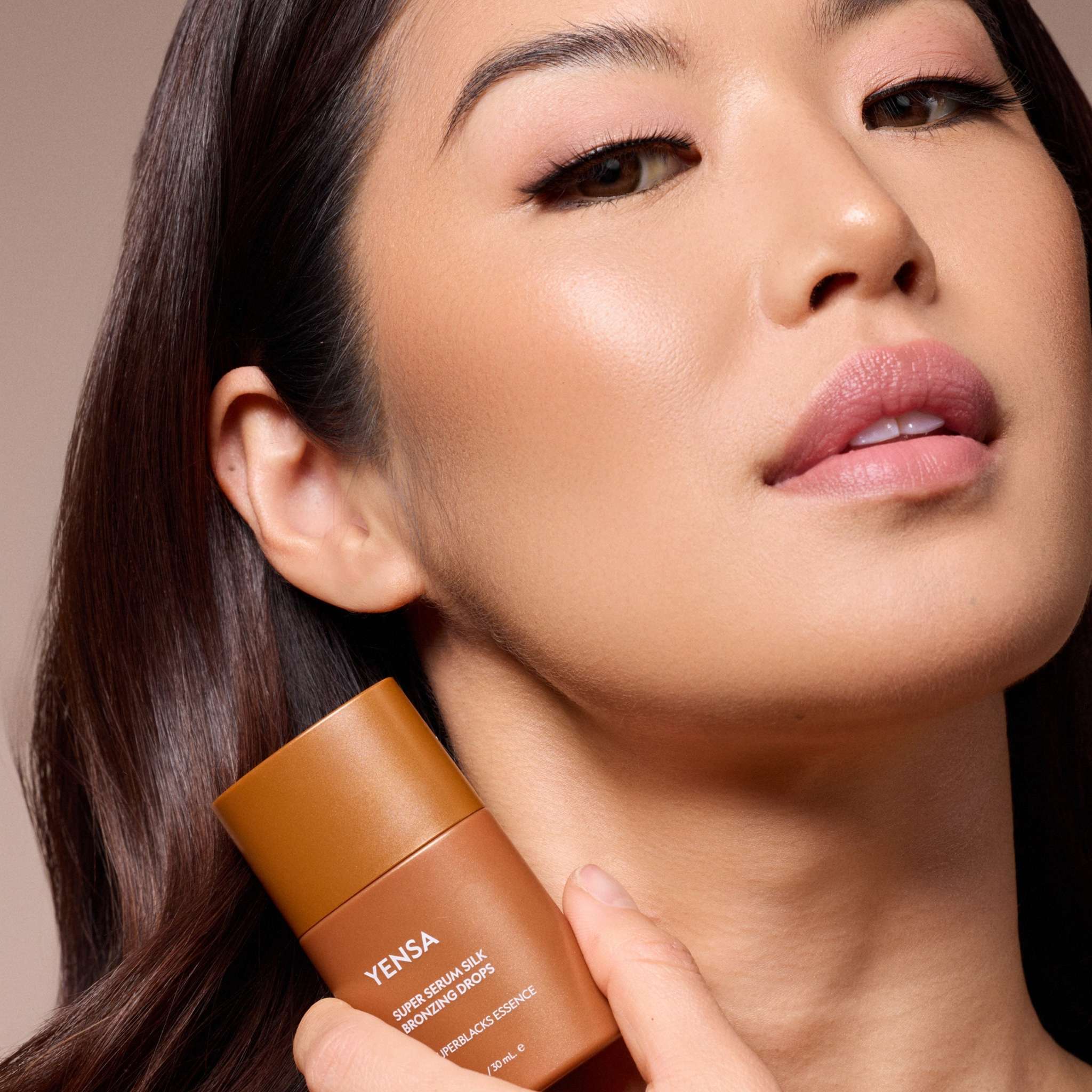 Super Serum Silk Bronzing Drops in a warm bronze bottle with a model showing smooth, radiant skin