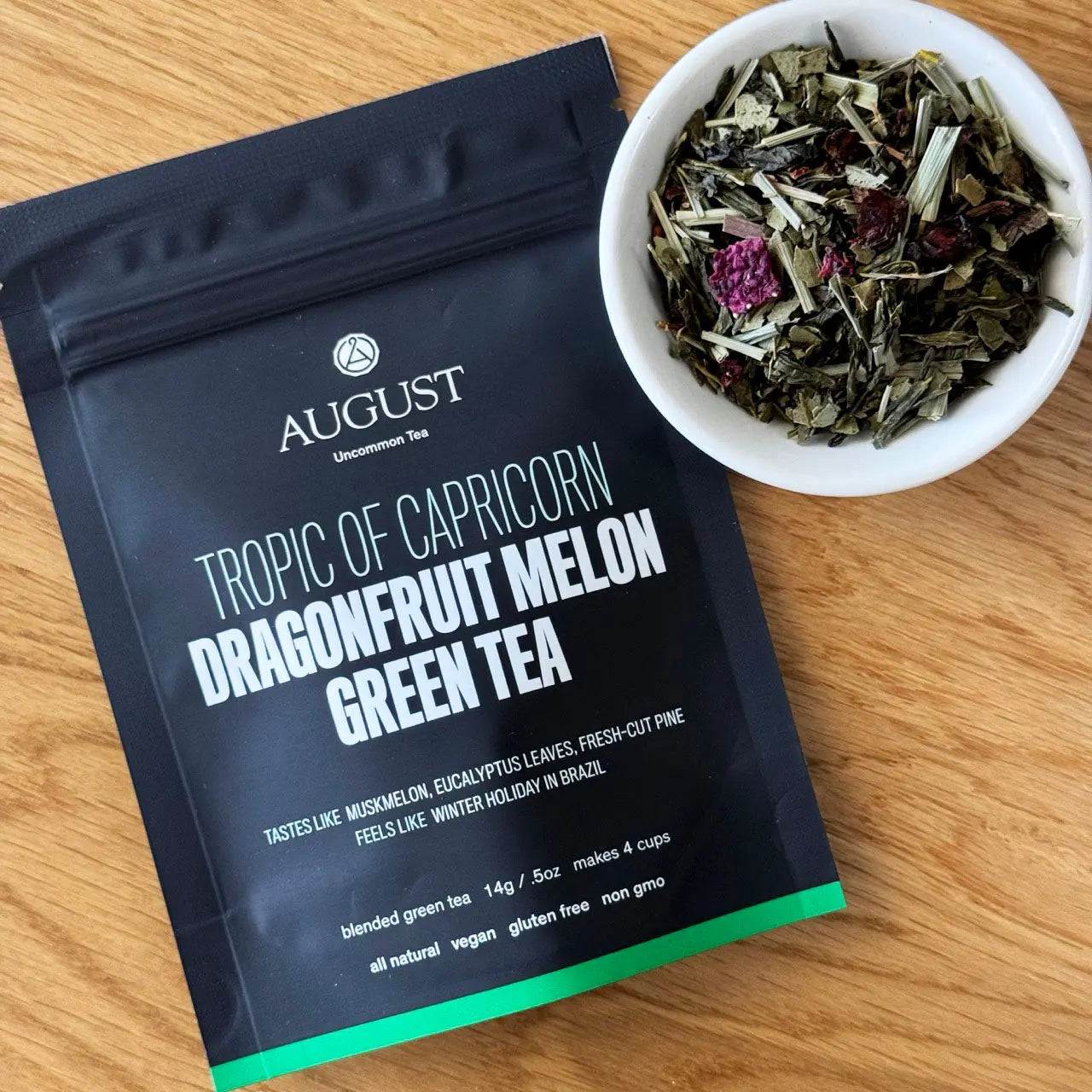 Tropic of Capricorn dragonfruit melon green tea in a black pouch with a bowl of loose green tea leaves