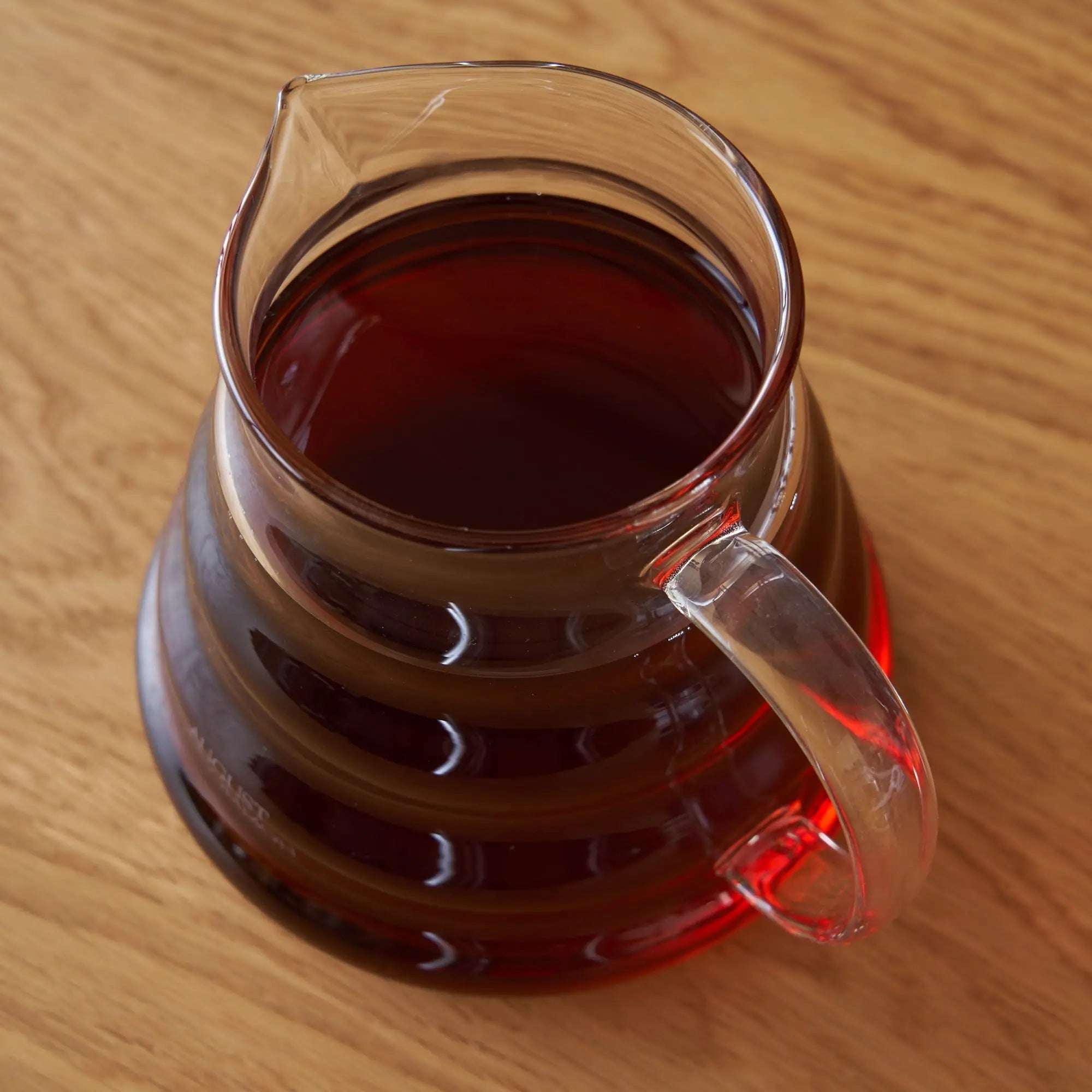 Two Cup Glass Teapot in clear heatproof glass, filled with dark amber tea and featuring a curved handle